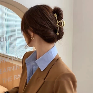 Détail d'une grande pince à cheveux flèche de Cupidon dorée portée sur un chignon élégant