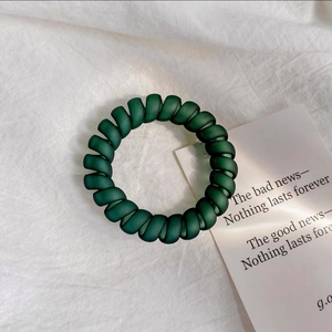 Gros plan sur un élastique spirale vert foncé mat sur fond en tissu texturé blanc