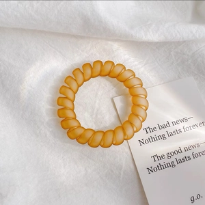 Vue détaillée d'un élastique spirale ambre mat posé sur un tissu de lin blanc minimaliste