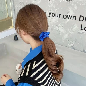 Close-up of a royal blue satin scrunchie worn on a ponytail with soft silk texture