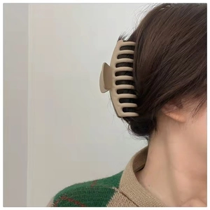 Detail view of a matte beige large hair claw clip styling a secure bun on a model