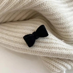 Detail shot of a black velvet bow hair clip resting on a white knitted texture fabric