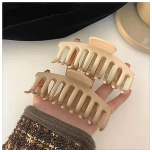 Detailed view of large matte hair claws in cream and khaki being held for size scale