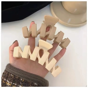 Close-up of two large matte hair claws in beige and coffee brown with geometric wavy design