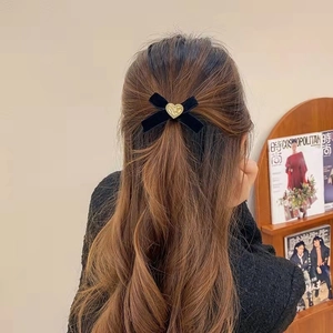 Barrette nœud en velours noir vintage avec cœur doré portée sur une coiffure mi-haute