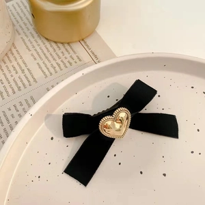 Détail de la barrette à nœud en velours noir avec une boucle en métal doré en forme de cœur