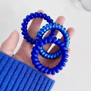 Trois élastiques à cheveux spirales bleu foncé montrés à la main, mats et brillants