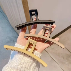 Hand holding three matte finish large claw clips in black, tan and beige tones