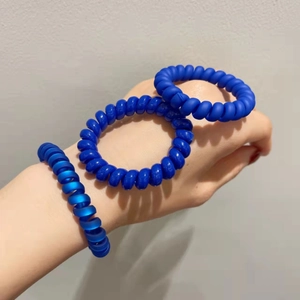 Gros plan d'élastiques à cheveux spirale bleu mat portés au poignet et à la main