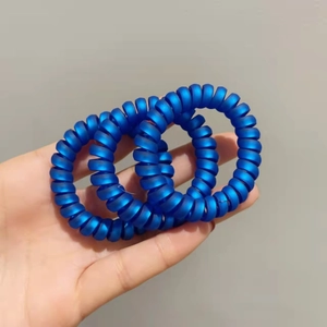 Gros plan de trois élastiques spirales bleu mat tenus à la main sur un fond gris neutre