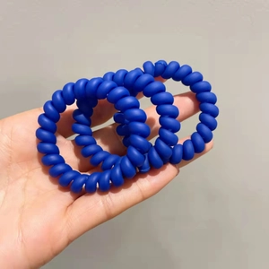 Vue détaillée de trois élastiques spirale bleu cobalt mat tenus en main pour le coiffage