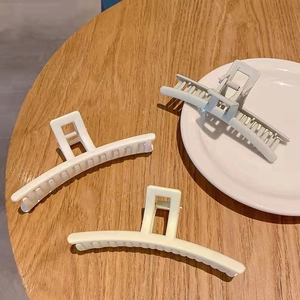 Detail view of large matte hair claws in beige, cream and blue on a wooden table