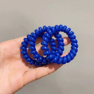Détail de trois élastiques spirale bleu foncé portés à la main en résine élastique