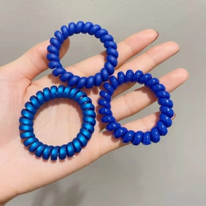 Détail de trois élastiques à cheveux spirales bleu foncé effet mat tenus dans la main