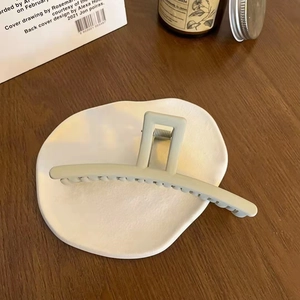 Matte bean green shark hair claw clip displayed on a minimalist ceramic tray detail