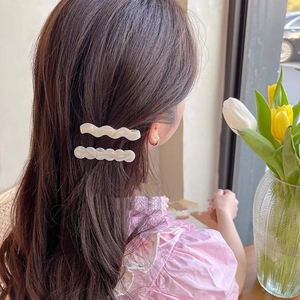 Élégantes barrettes à cheveux ondulées en résine nacrée portées par une femme à la fenêtre