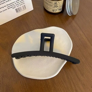 Close-up of matte black shark hair claw clip on ceramic tray with wooden background