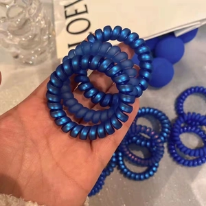 Gros plan sur l'élastique cheveux spirale bleu Klein mat tenu en main au fini doux