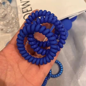 Gros plan de trois chouchous spirales bleu Klein en fil de téléphone dans la main