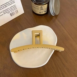 Matte ginger yellow hair claw clip shown on white ceramic tray in a cozy lifestyle setting