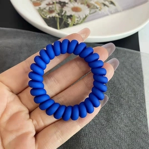 Vue détaillée d'un élastique spirale bleu Klein mat pour cheveux tenu à la main