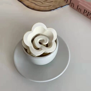 Dettaglio del fermaglio a fiore color crema con finitura opaca in una tazza