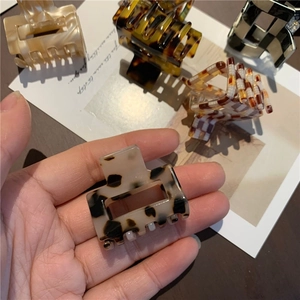 Detail shot of leopard and checkerboard acetate hair claws held in hand for scale