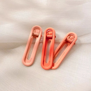 Close-up of three gradient orange matte hair clips with hollow design on white mesh fabric