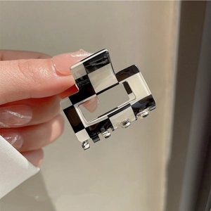 Detail of a small black and white checkered acetate hair claw clip held by hand