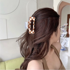 Brown and white checkerboard acetate hair claw clip worn by a model in a cozy home setting