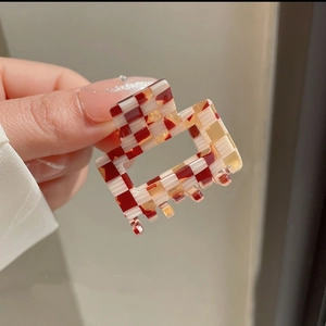 Close-up of a red and cream checkered acetate square hair claw clip held by fingers