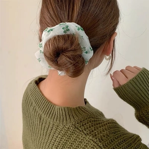 Dettaglio di elastico per capelli con fiori verdi indossato su uno chignon morbido