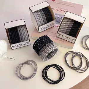 Detail of high-elasticity braided hair ties in black and gray stored in a white box