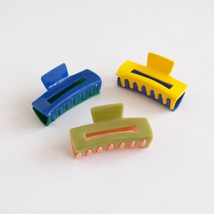 Three minimalist rectangular hair claw clips in bold contrasting colors on beige background