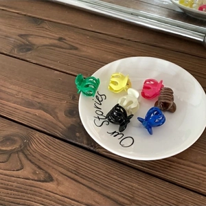 Colorful mini resin hair claws displayed in a stylish white dish on a wooden table