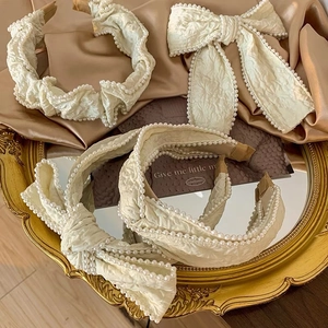 Elegant cream-colored bow headband with pearls on a vintage gold mirror surface