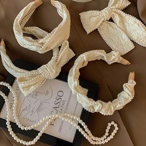Detail of creamy white headband with pleated fabric texture and delicate pearl trim