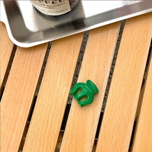 Close-up of a mini vibrant green hair claw clip on a light wood background for daily use