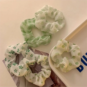 Dettaglio di elastici per capelli in tessuto verde con motivi a quadri, fiori e pois