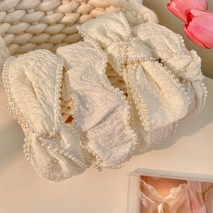 Close-up of cream white bow headband with pearl edges and floral textured fabric detail