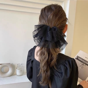 Détail d'un chouchou élégant en dentelle noire à pois blancs sur cheveux bouclés