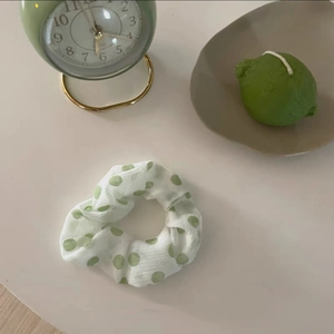 Dettaglio dell'elastico per capelli a pois verdi su un tavolo minimalista