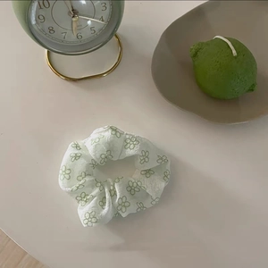 Dettaglio dello scrunchie bianco con ricamo di fiori verdi su tessuto leggero