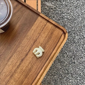 Top view of a mini cream-white resin hair claw clip on a wooden tray for daily styling