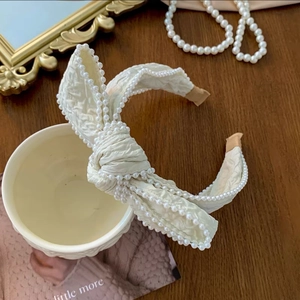 Close-up of cream bow headband with delicate pearls and soft pleated fabric texture