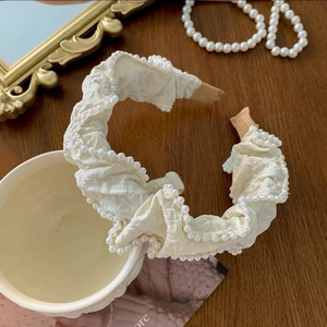 Detailed view of cream white headband with pleated fabric and white pearls on ceramic cup