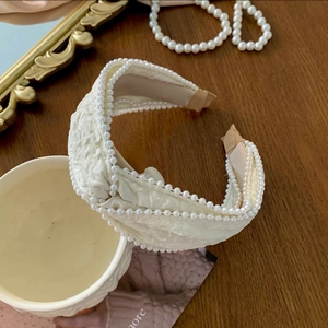 Close-up of cream twisted headband featuring elegant white pearl edging on a wood desk