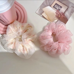 Détail de chouchous en organza fleuri crème et rose sur un fond doux et élégant