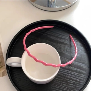 Close-up of a pink wavy-textured hairband leaning on a ceramic mug over a black tray