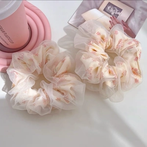 Détail de chouchous floraux géants en tulle avec motifs de fleurs roses sur table blanche
